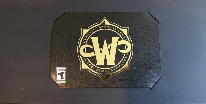 A black rectangular box with a gold logo in the center. The logo features two intertwined "W" letters and the text "THE WORLD OF WARCRAFT". A "T" rating symbol is visible in the bottom left corner.